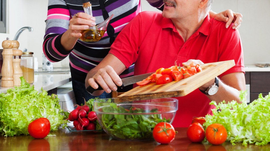 elderly couple cooking with tomatoes in home kitchen